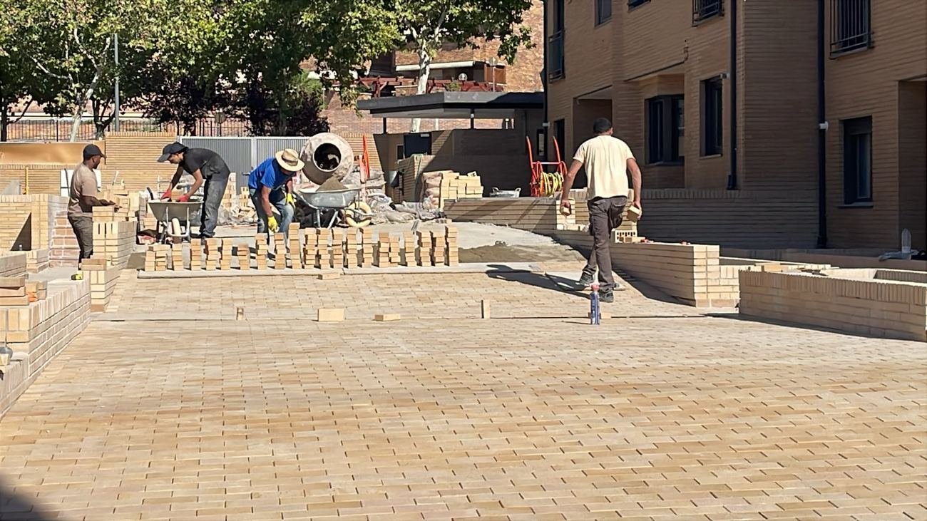 Equipo colocando adoquín y levantando muretes de caravista en un patio de viviendas